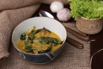 Catfish Curry with Cumin Leaves served in an art-patterned cup. On a brown wooden table.