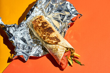 Shawarma roll in foil on a bright orange background