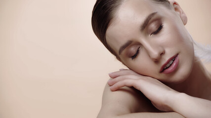 Naklejka premium feather near cheek of young woman with closed eyes isolated on beige.