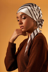 A portrait shot of a swarthy pretty lady in a brown jumper and a white silk head scarf with a brown...
