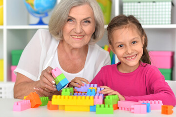 Cute girl and grandmother playing with colorful plastic blocks