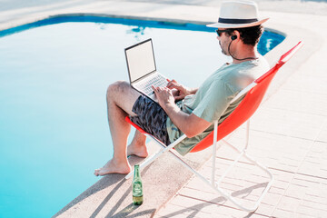 man sitting on beach chair by the swimming pool with a laptop and beer alone