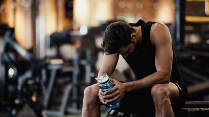 sportsman in earphone listening music, resting and holding sports bottle in gym. - Powered by Adobe