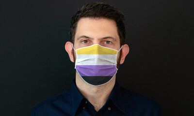 Portrait of an adult man wearing a LGBT non-binary flag colors facial mask. LGBT gay rights concept with black background. These colors symbolize the non-binary flag.