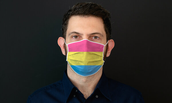 Portrait Of An Adult Man Wearing A LGBT Pansexual Flag Colors Facial Mask. LGBT Gay Rights Concept With Black Background. These Colors Symbolize The Pansexual Flag.