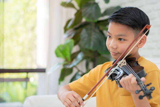 A Little Asian kid playing and practice violin musical string instrument against in home, Concept of Musical education, Inspiration, Teenager art school student.