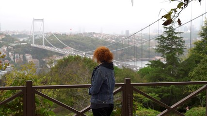 Turkish woman looking at Istanbul skyline with Fatih Sultan Mehmet Bridge. Also known as the Second Bosphorus Bridge, it spans the Bosphorus strait, Istanbul, Turkey.