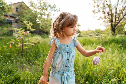 Easter egg hunt. Girl child running to pick up Egg in Garden. Easter tradition. Baby with basket full of colorful eggs.