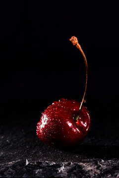 one red cherry with water drops on a black stone background