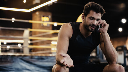 Naklejka premium young sportsman talking on smartphone and gesturing in gym.
