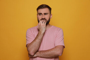 Man biting his nails on yellow background. Bad habit