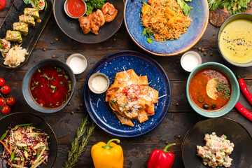 pasta with tomatoes, salmon rolls, vegetable soup, salyanka soup, olivier salad top view on a wooden background