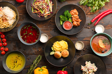 mashed potatoes with meat balls, pasta with tomatoes, salmon rolls, vegetable soup, salyanka soup, borsch soup top view on a wooden background