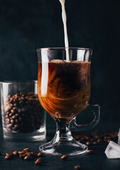 close-up on coffee with milk in a transparent glass against the background of coffee beans on a black background