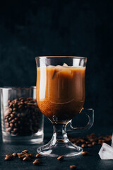 close-up on coffee with milk in a transparent glass against the background of coffee beans on a black background