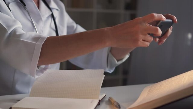 Medical information. Junior physician. Mobile technology. Unrecognizable woman making photo encyclopedia data on smartphone sitting light room interior.