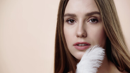 Naklejka premium sensual young woman near soft feather isolated on beige.