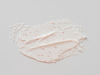 Scrub smears isolated on white background. Texture cosmetic scrub for face and body with red abrasive particles in pastel pink color. Exfoliating body polish texture as cosmetic gommage background - obrazy, fototapety, plakaty