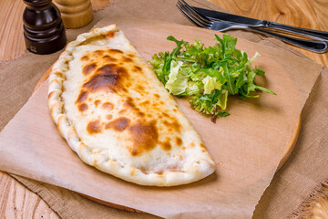 Closed calzone pizza with ham and cheese on the board