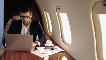 Fototapeta premium Businessman using laptop near coffee and smartphone in private jet.