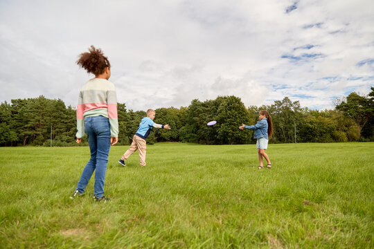 childhood, leisure and people concept - group of happy children playing game with flying disc at park