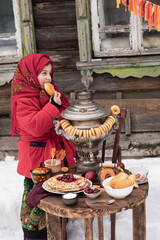 A joyfool girl bites pie in traditional clothes with a stack of pancakes, samovar. Maslenitsa .Shrovetide concept