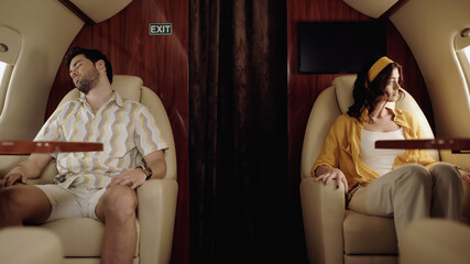 Young woman sitting near boyfriend sleeping in private plane.
