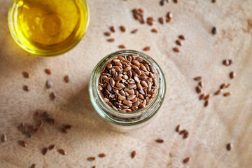 Fresh flax seeds in a jar, with flax seed oil in the background