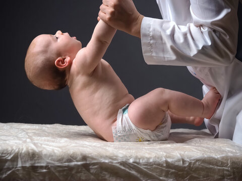 doctor lifts the hands of the baby lying on the table checking the reflexes of the newborn