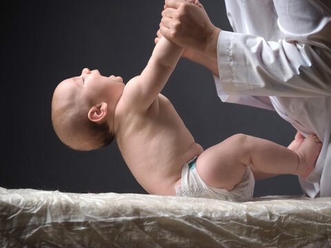 doctor lifts the hands of the baby lying on the table checking the reflexes of the newborn