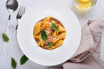 Bolognese Penne Pasta. Tasty appetizing classic italian penne pasta with parmesan cheese, basil and Bolognese sauce in white plate on plate on stone table Traditional dish of Italian cuisine. Top view