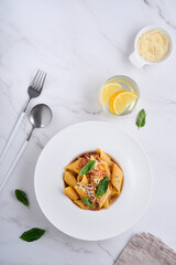 Bolognese Penne Pasta. Tasty appetizing classic italian penne pasta with parmesan cheese, basil and Bolognese sauce in white plate on plate on stone table Traditional dish of Italian cuisine. Top view