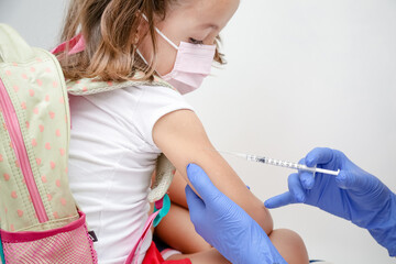 Criança sendo vacinada contra covid 19 volta as aulas medica com luva azul e seringa.
