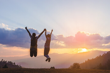 Silhouette of happy two teenage girls jumping on mountain sunset background.