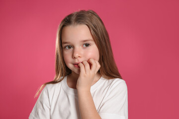 Cute little girl biting her nails on pink background