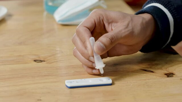 4K, Close Up Asian man's hands dropping fluid on COVID-19 specimen test strip. coronavirus pandemic protection concept.  the test a rapid antigen test kit to self-test the COVID-19 epidemic at home