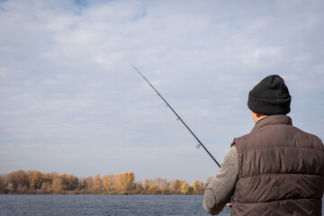 A man with a fishing rod fishing on the background of the river. Fishing relaxation concept