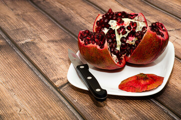 White plate with cut ripe pomegranate on a wooden table. The concept of proper nutrition. Close-up, space for text