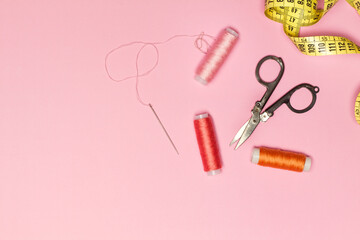 Hilos de colores junto a una tijera, cinta métrica, y una aguja enhebrada sobre un fondo rosa pastel liso y aislado. Vista superior. Copy space