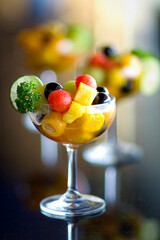 Fresh fruit salad in cocktails glass on black stone background.