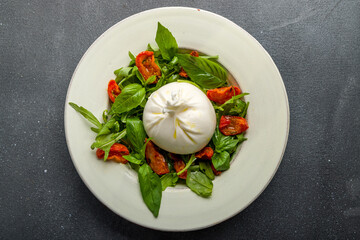 Salad with buratta cheese, sun dried tomatoes and greens on grey concrete table top view