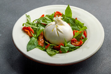 Salad with buratta cheese, sun dried tomatoes and greens on grey concrete table
