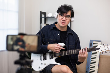 Young asian musician teaching the rock guitar class online live streaming on smartphone with...