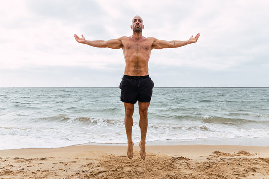 Shirtless sportsman jumping on sandy beach