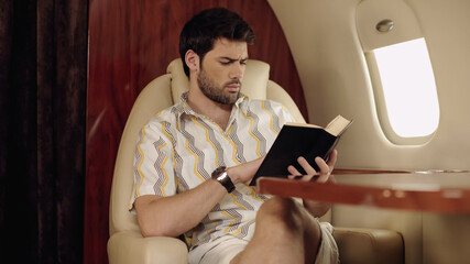 Bearded man reading book while traveling in private jet.