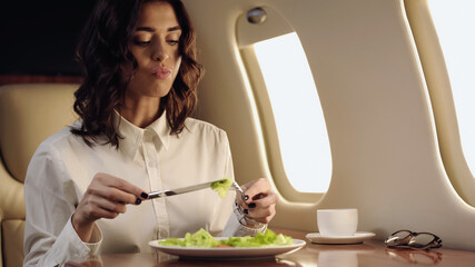 Fototapeta Businesswoman holding cutlery near blurred salad and coffee in private jet. obraz