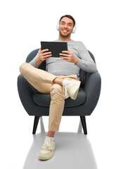 people, technology and music concept - happy smiling man with headphones and tablet pc computer sitting in chair over white background