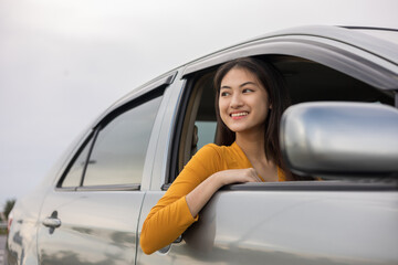 Young beautiful asian women getting new car. she very happy and excited looking outside window. Smiling female driving vehicle on the road on a bright day