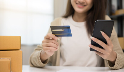 Shopping online. Young asian woman input the serial number of credit card to smartphone for shopping payment. Buying online at home. Small business entrepreneur with many parcel box on table
