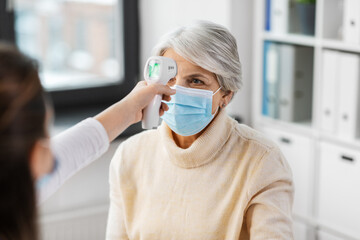 medicine, health and pandemic concept - doctor with infrared thermometer gun checking senior...